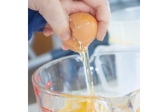 Image A hand cracking an egg into a glass bowl.
